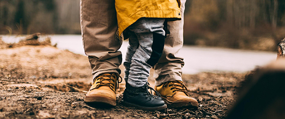 view of father and toddler from foot to knee, standing in forest